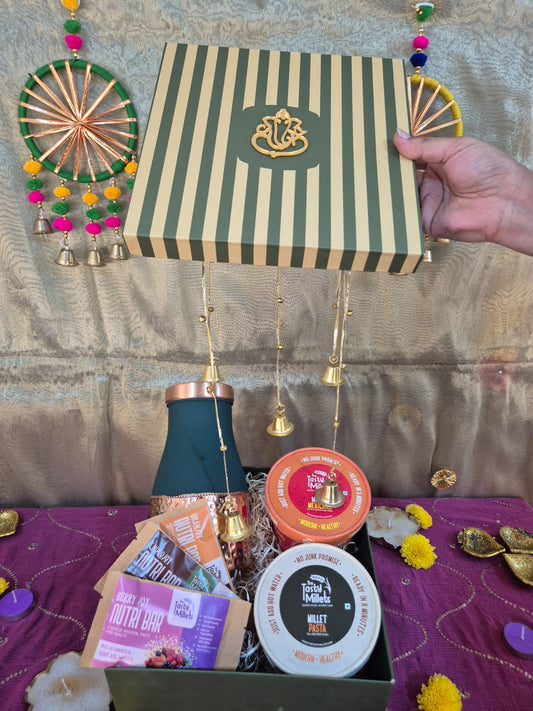 Green striped gift box with gold emblem above a festive basket of snacks and assorted gifts.