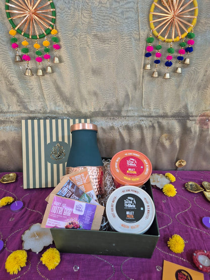Green striped gift box with gold emblem above a festive basket of snacks and assorted gifts.