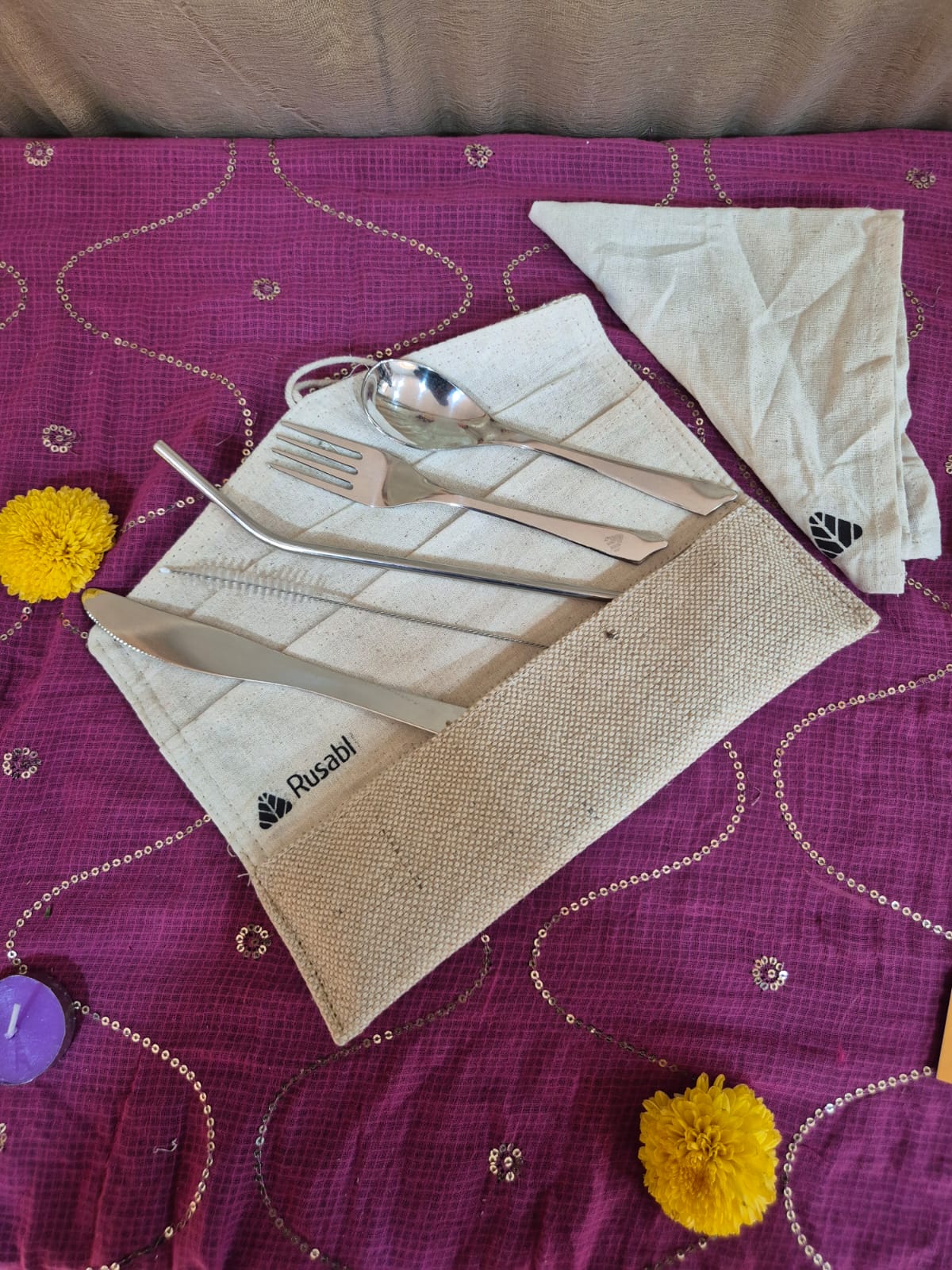 Reusable metal cutlery set with beige woven pouch and matching napkin on purple fabric.
