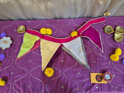 Handmade fabric bunting with colorful triangular flags and marigold flowers on purple fabric.